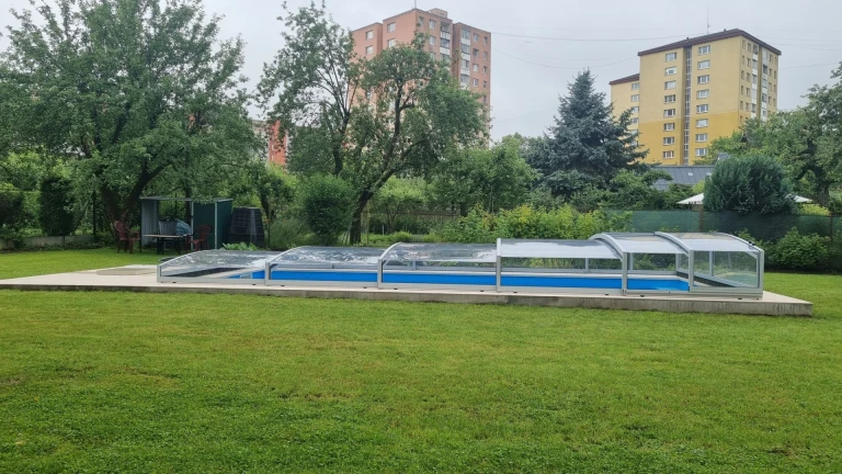 Alacsony PREMIER medencefedés egy martini kertben, zöld pázsittal és háttérben látható lakóházakkal