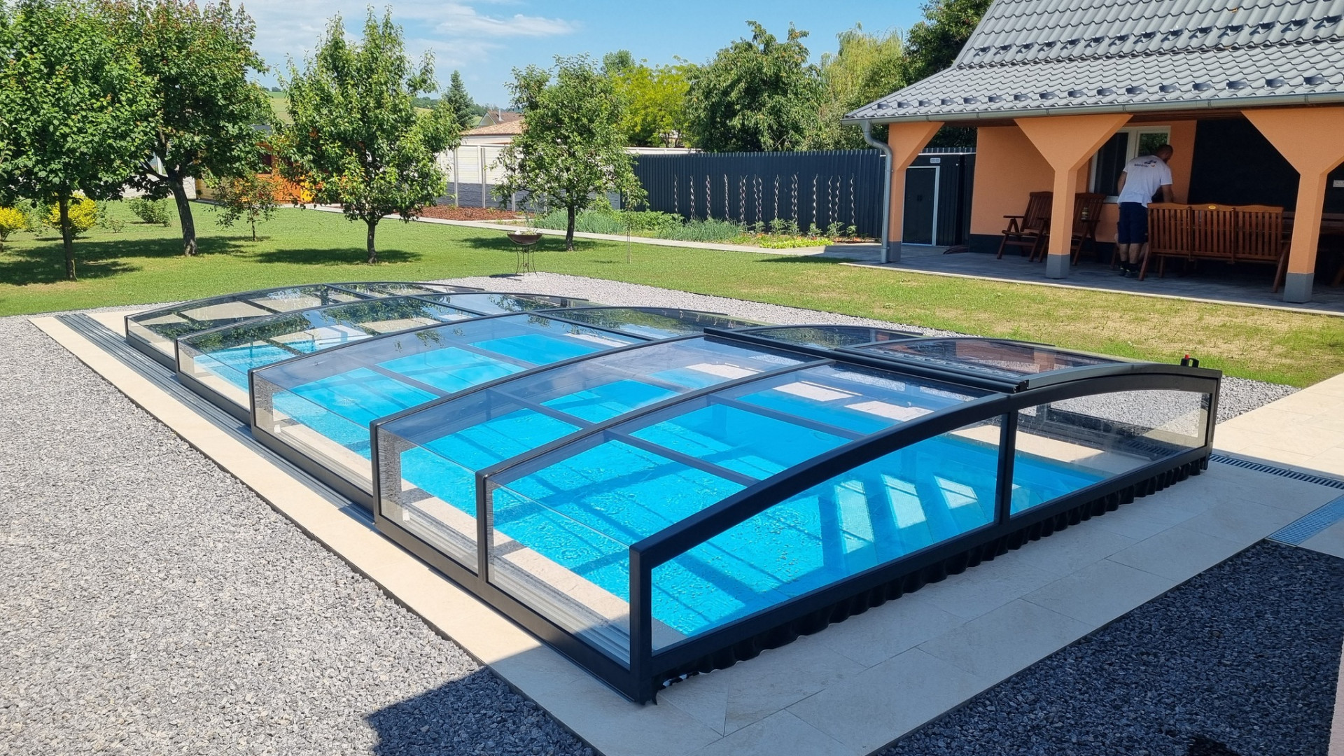 Modern, alacsony PREMIER medencefedél s sötét kerettel egy családi ház kertjében.