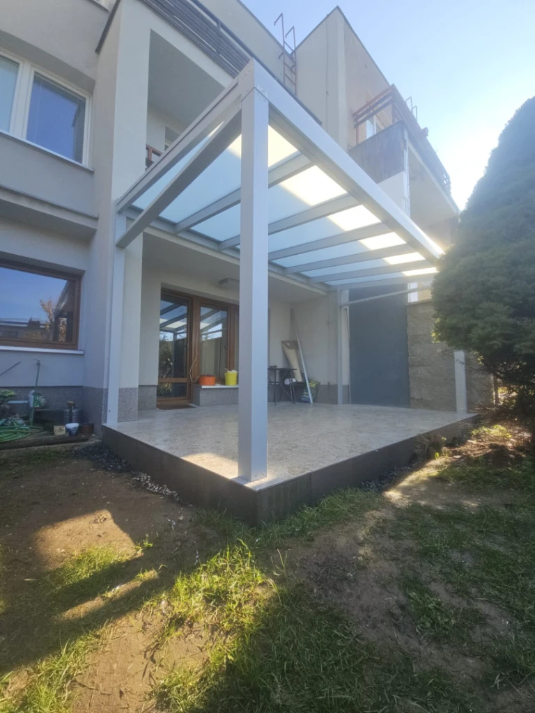 Egy családi ház teraszán felépített, modern, fehér alumínium pergola tejfehér üvegezéssel