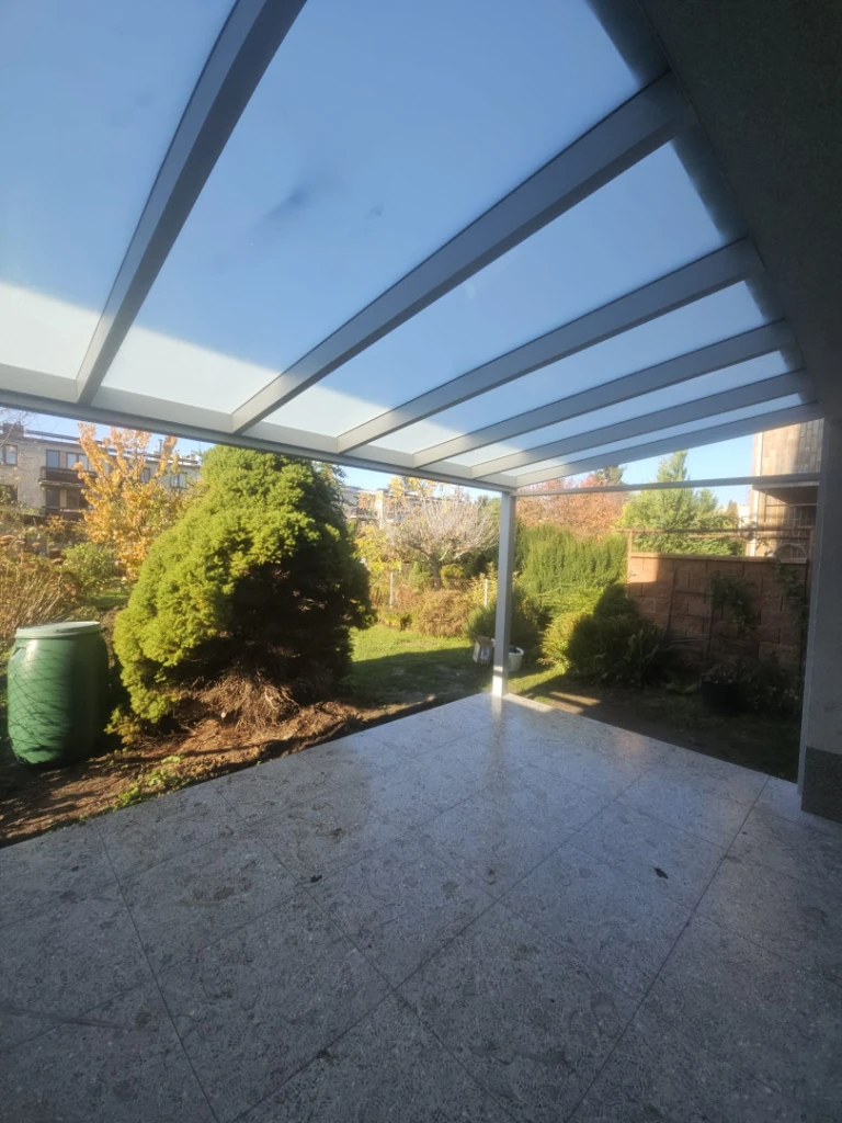 Modern alumínium pergola üvegtetővel a terasz felett, kilátással a kertre.