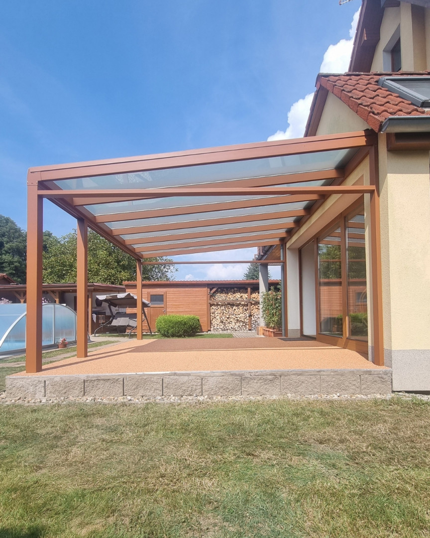 Egy családi házhoz csatlakozó, barna alumínium pergola üvegtetővel