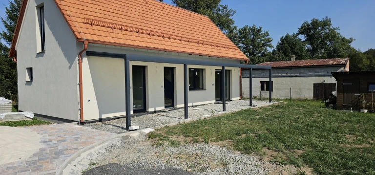 Egy új építésű, narancssárga tetős családi házhoz épített, modern, sötét szürke alumínium pergola.