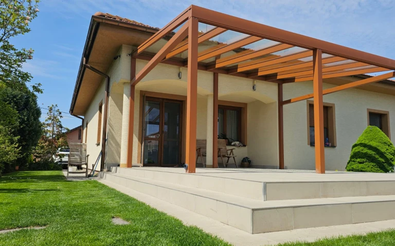 Barna alumínium pergola üvegtetővel, egy családi ház teraszára szerelve