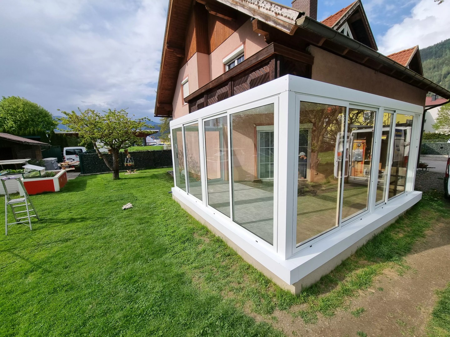Egy családi ház kertjében álló, modern, fehér, üvegezett alumínium pergola.