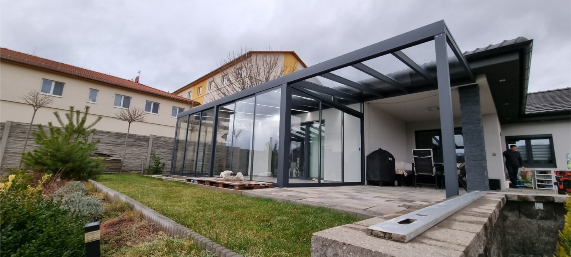 Egy modern, üvegezett alumínium pergola antracit színű vázzal, amelyet egy családi ház mellett építettek Kláštercben.