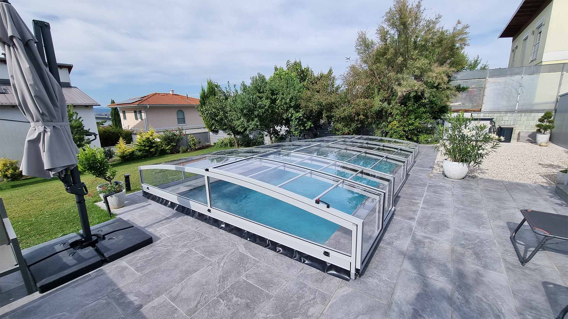 A PREMIER modern, alacsony alumínium medencefedél egy családi ház kertjében, a burkolt teraszon
