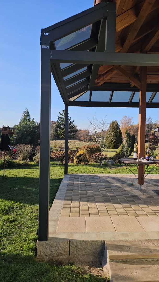Részletes képet ad az alumínium szerkezetről és a pergola üvegezett tetőjéről, ahonnan kilátás nyílik a kertre.