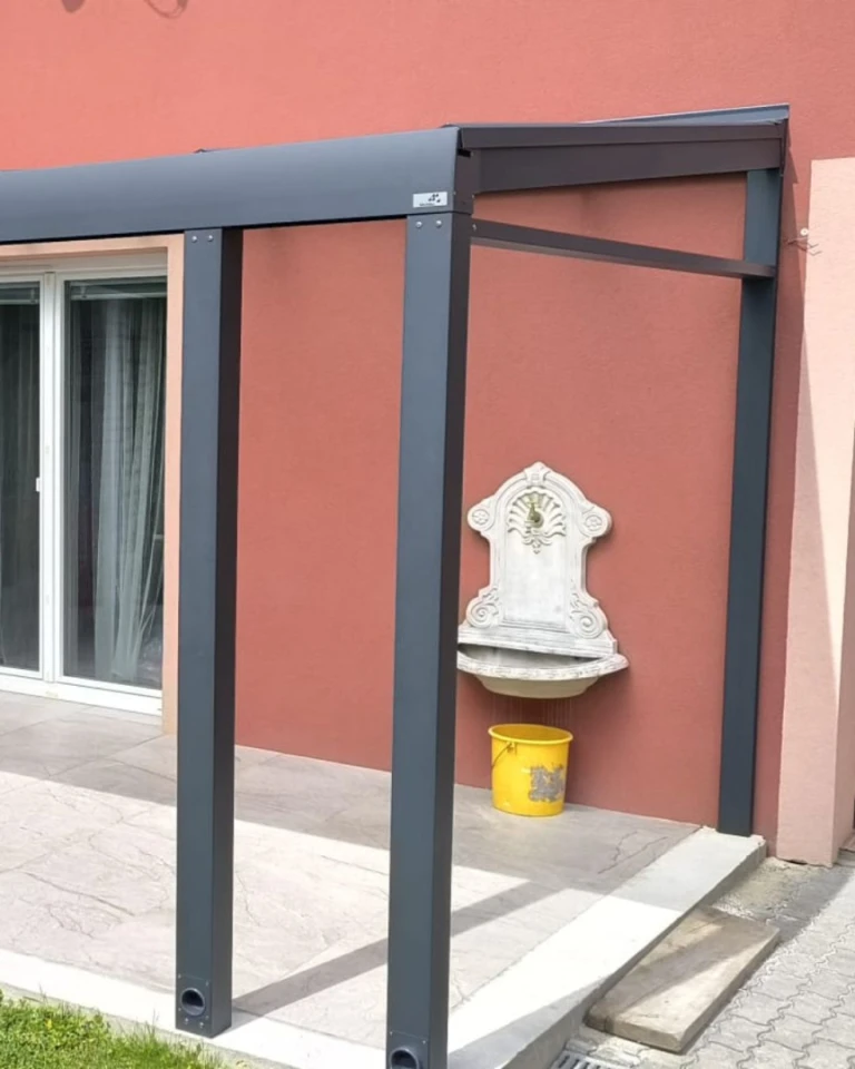 Részletes képet nyújt a teherhordó szerkezetről és az alumínium pergola csatlakozásáról a ház homlokzatához, díszes mosdóval.