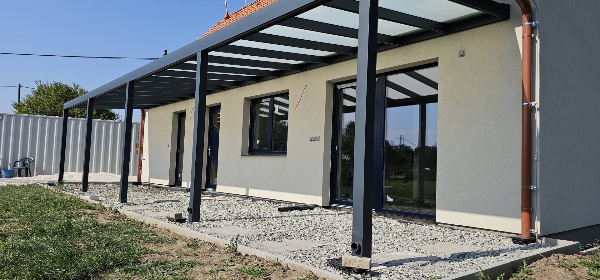 Egy családi ház falához rögzített, üvegtetős, modern alumínium pergola