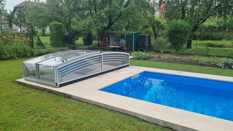 Modern, alacsony medencefedés átlátszó burkolattal a kertben található nyitott medence mellett.