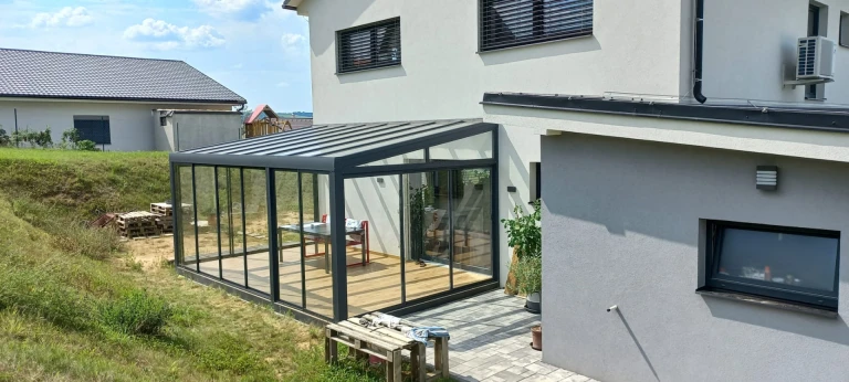 Egy családi házhoz épített, modern, üvegezett télikert sötét vázszerkezettel