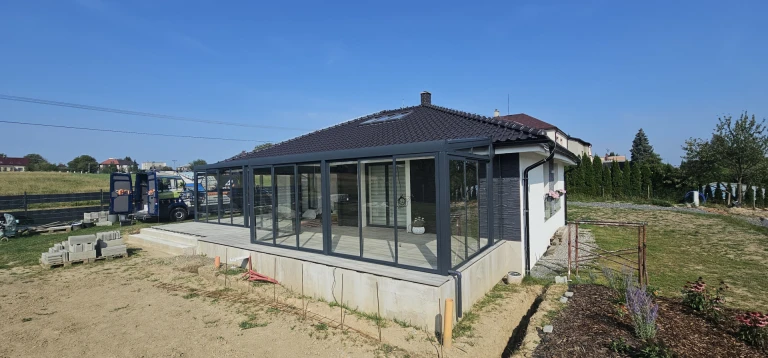 Egy családi ház mellé épített, modern, üvegezett télikert antracit színű szerkezettel